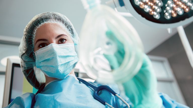 Anaesthetic nurse in an operating theatre holding an oxygen or anaesthetic gas mask.