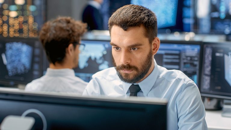 Data science professional working at multiple computer monitors in a modern high-tech office environment.