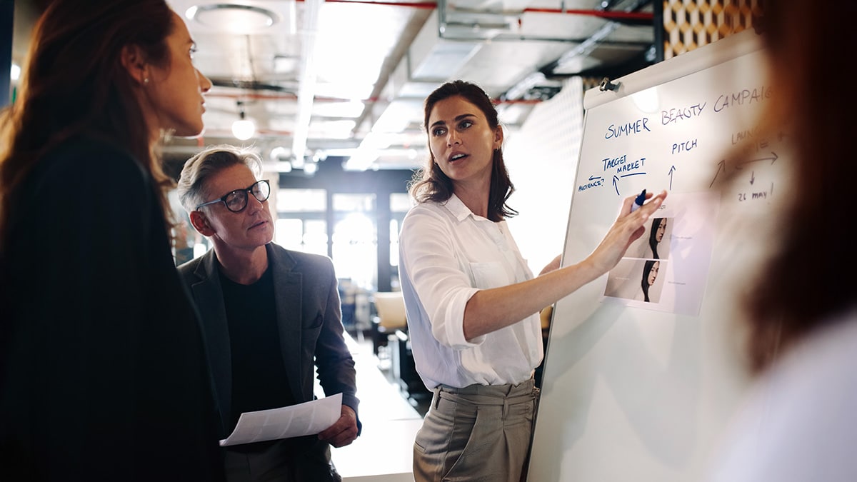 Marketing professional presenting a campaign strategy to colleagues using a whiteboard.