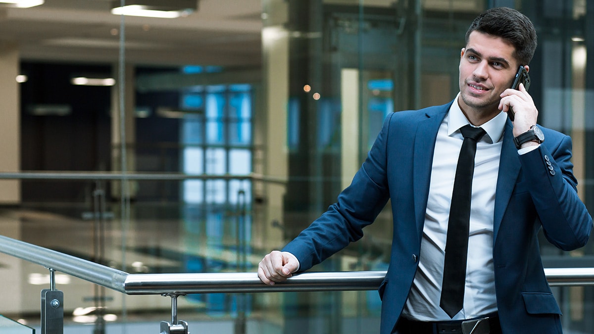 Man in a blue suit speaking on a mobile phone in a modern office building.