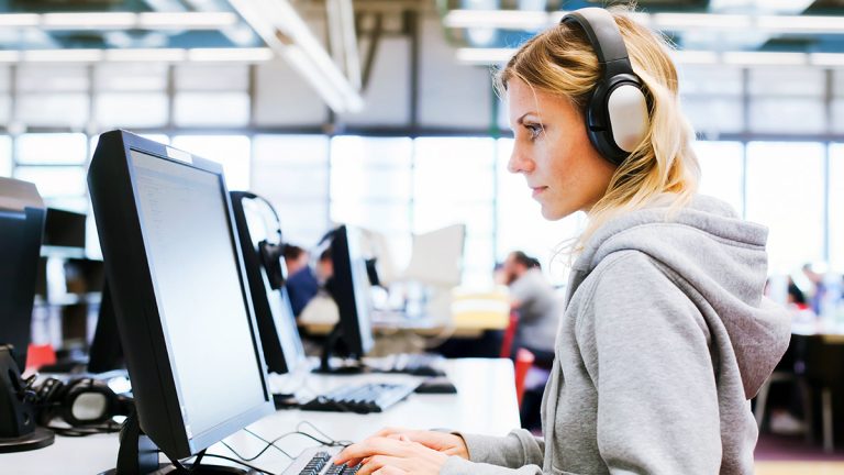 Woman wearing headphones studying human resource management online at a desktop computer