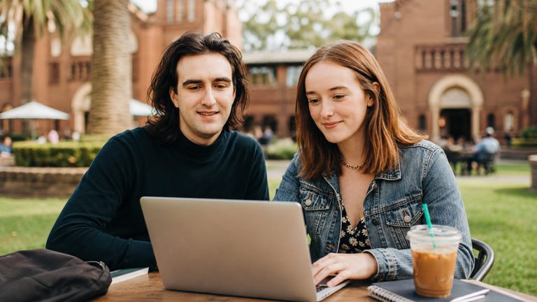 Two students studying on a laptop outdoors on a university campus, illustrating the ACU Online Graduate Diploma in Psychology course review.