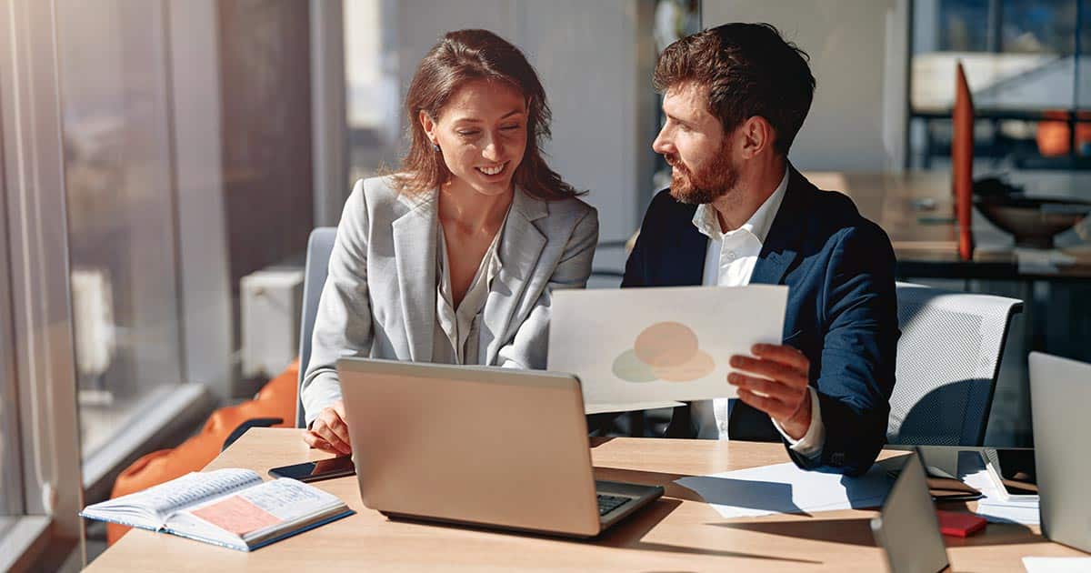 Male and female professionals discussing chart over laptop at work