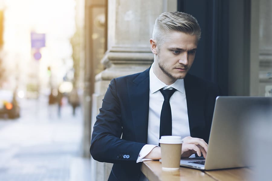 Male professional working on laptop with coffee outside cafe