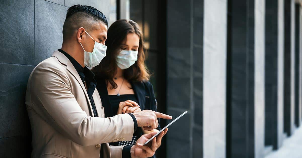 Male and female professionals wearing masks and looking at computer tablet