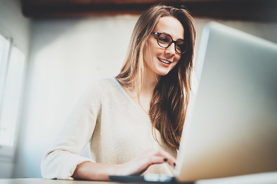 Smiling woman with glasses using a computer with a large screen