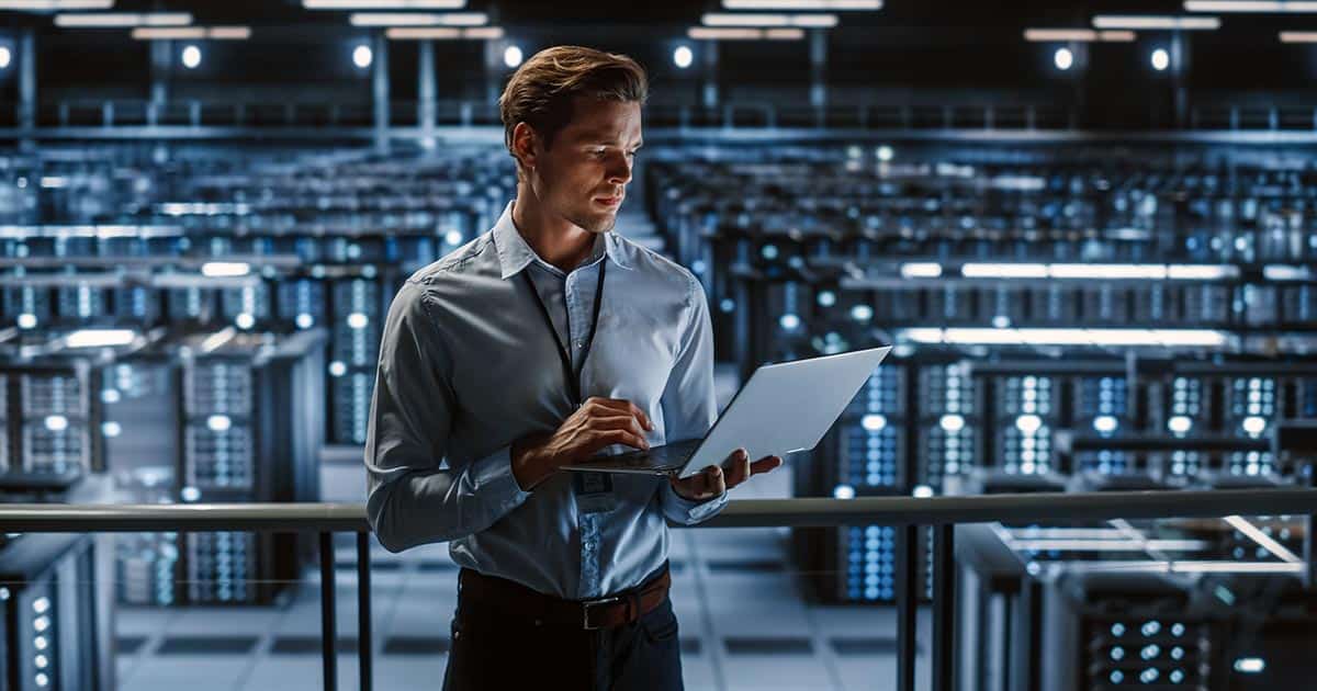 Professional man with laptop standing in front of stacks of servers