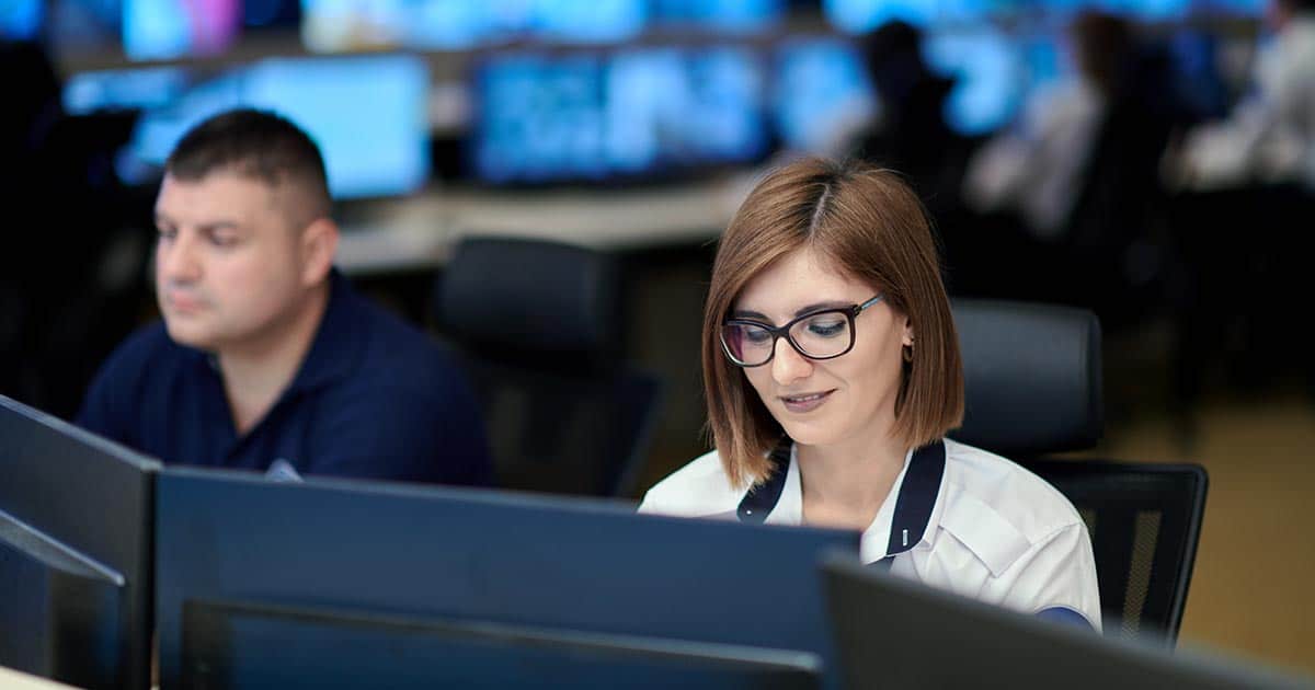 People sitting at desks in office with large computer screens