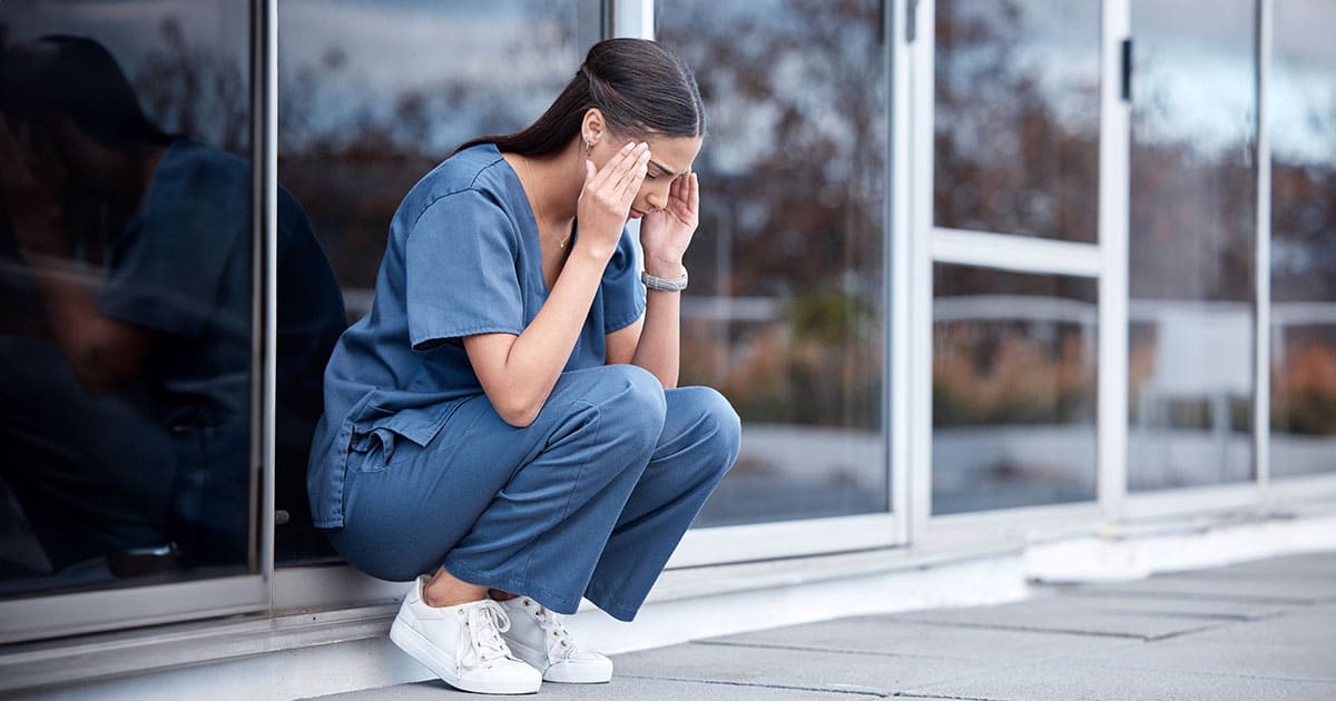 Dejected-looking woman in scrubs outside building