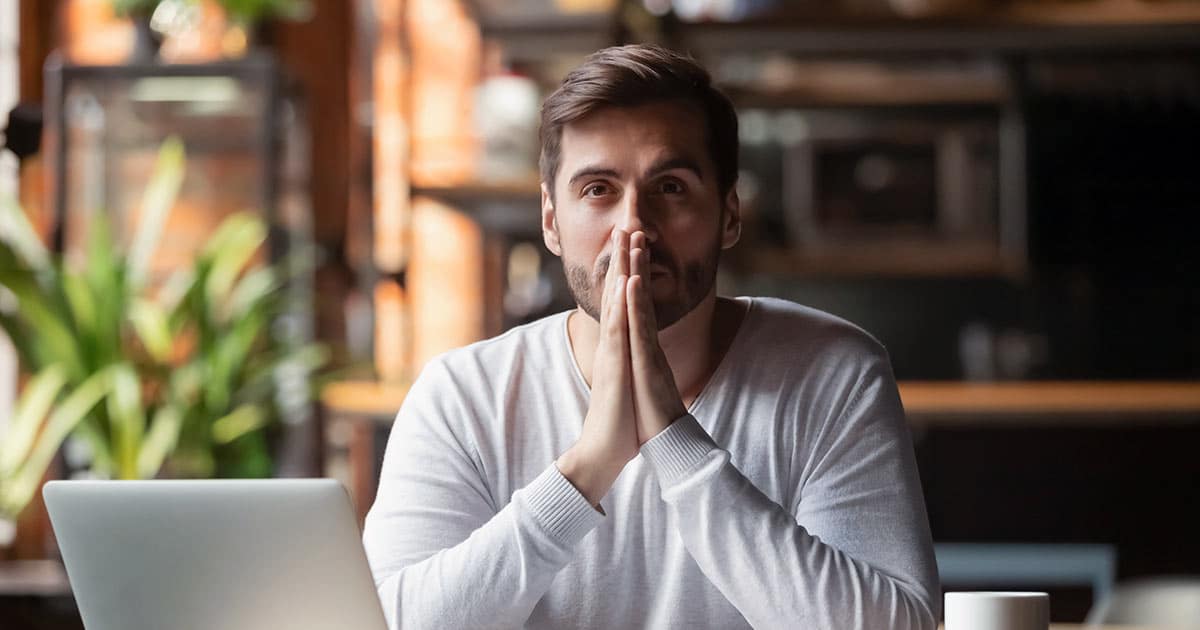 Difficult decision for man with hands clasped near laptop