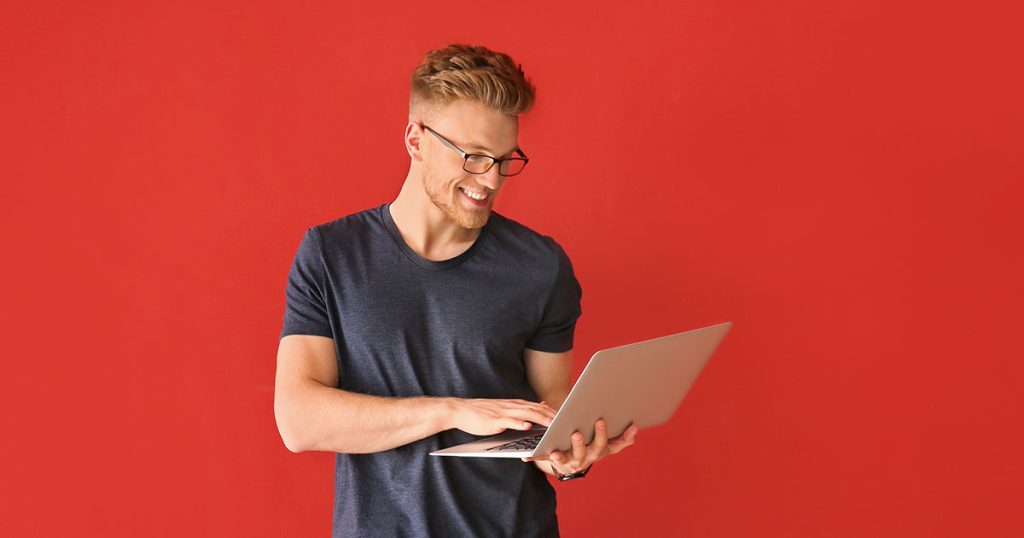 Young man wearing glasses using laptop standing up