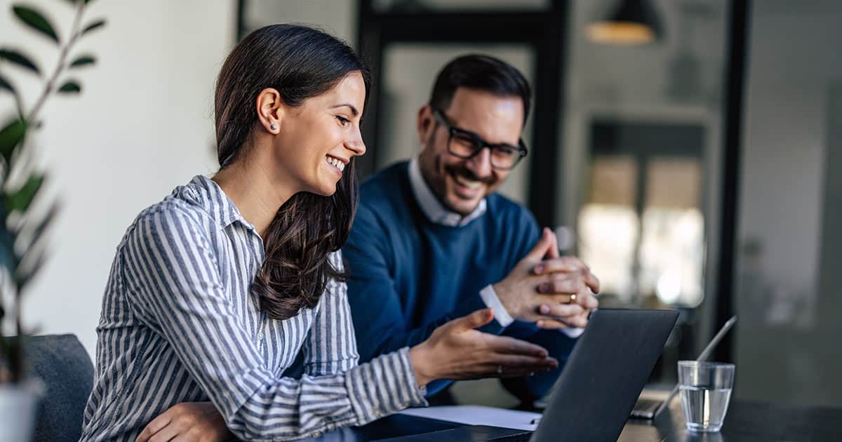 A female and male professional laughing at laptop display