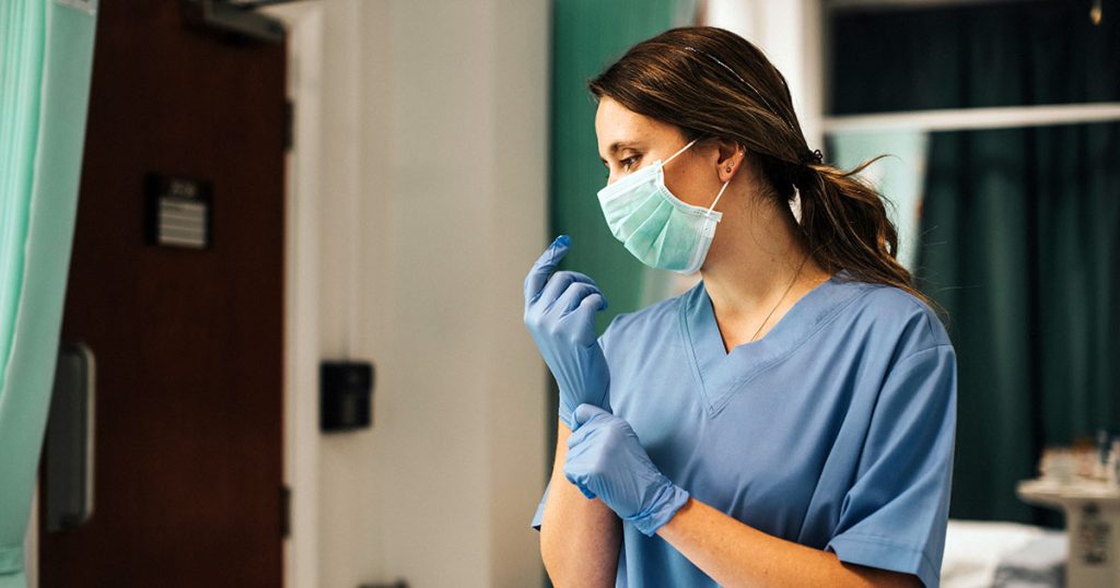 Female nurse with a mask putting on gloves