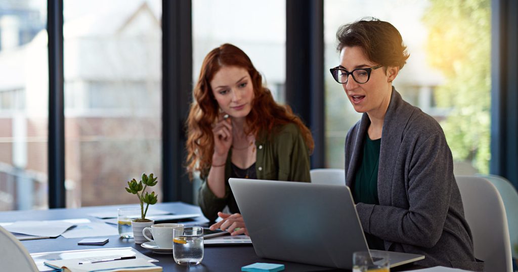 Female professionals consulting over laptop in large office suite