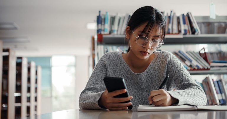 Female university student writing notes in library