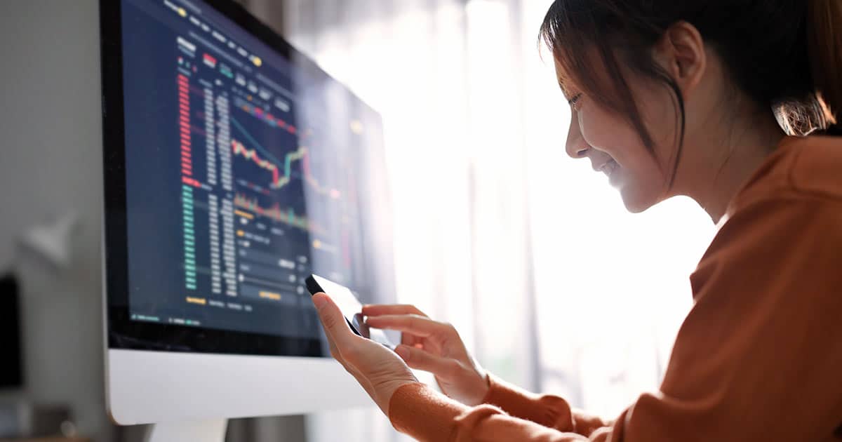 Woman on phone in front of large computer screen showing financial business charts