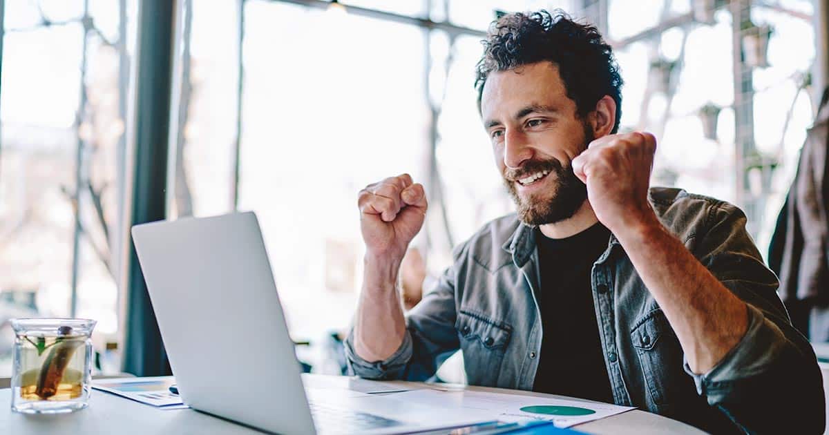 Jubilant man smiling at laptop with printed chart in front