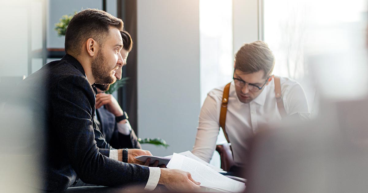 Three professionals looking at documents in a small-table meeting