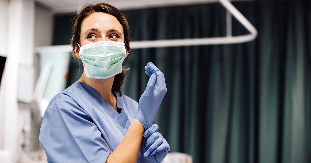 Woman in blue scrubs putting on surgical gloves