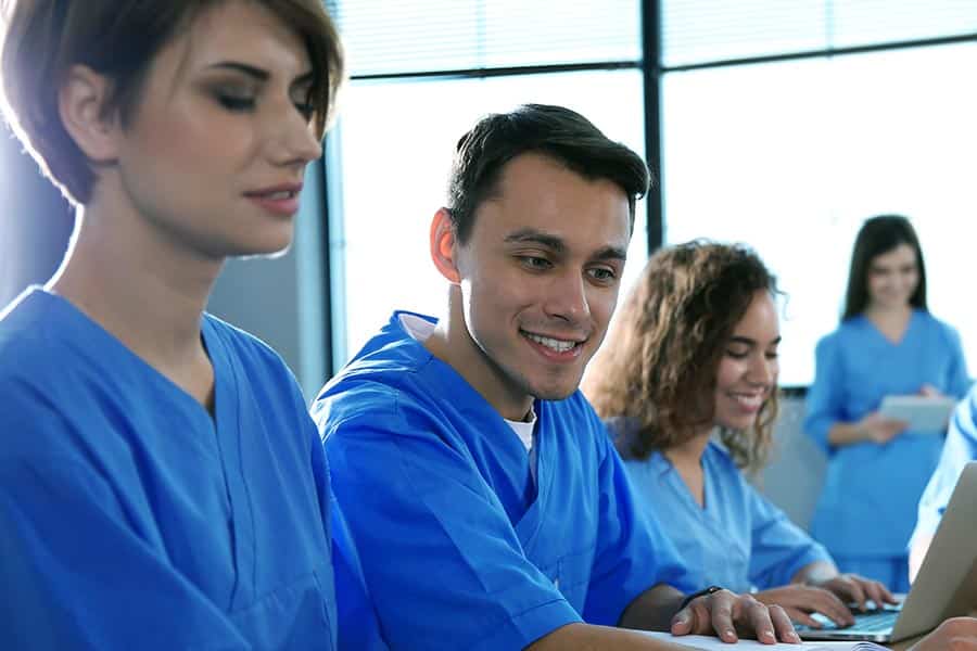 Group of young adults in blue scrubs sitting at meeting table