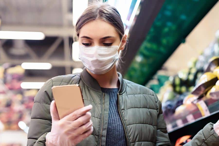 Woman wearing mask while shopping in supermarket and checking phone