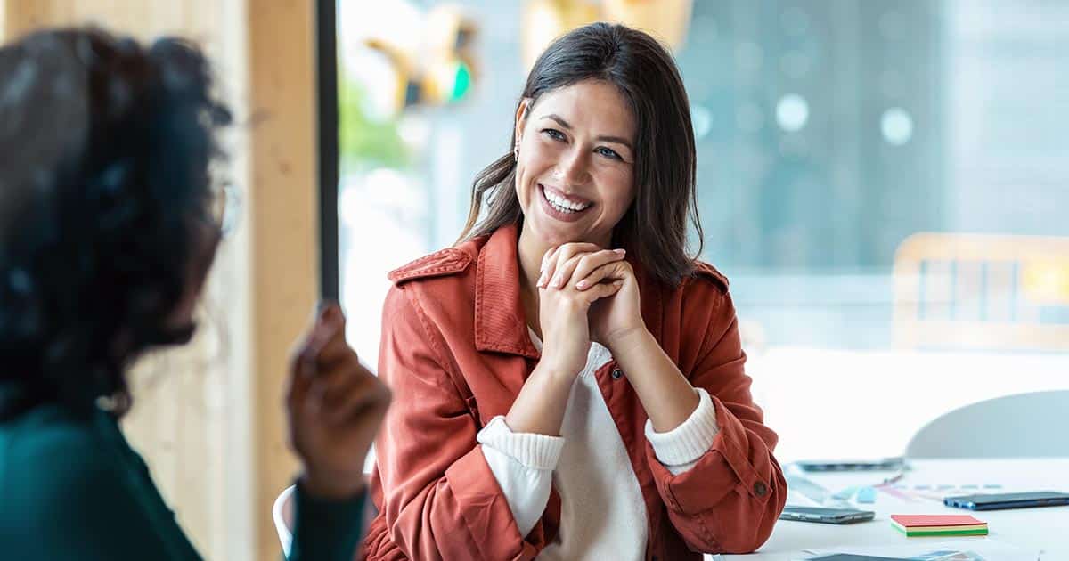 Woman at desk smiling in conversation with another woman