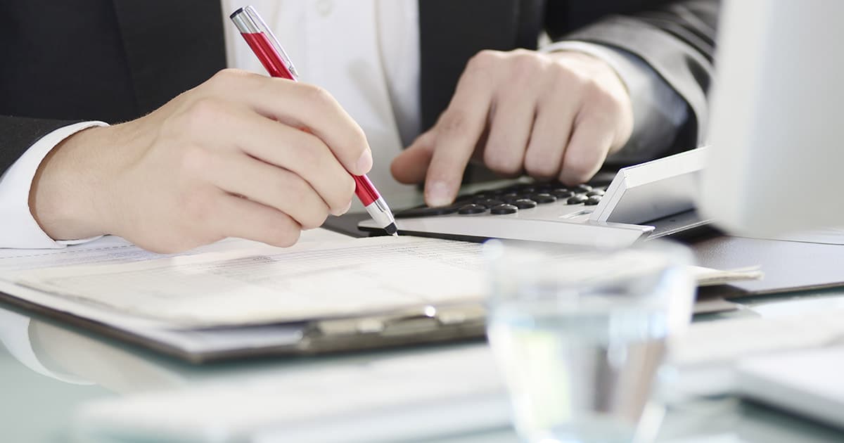 Businessman at desk with clipboard using pen and computer