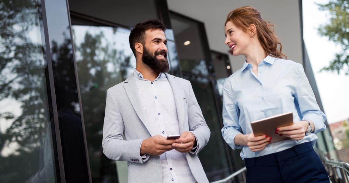 Male and female professionals walking and talking with devices outside building