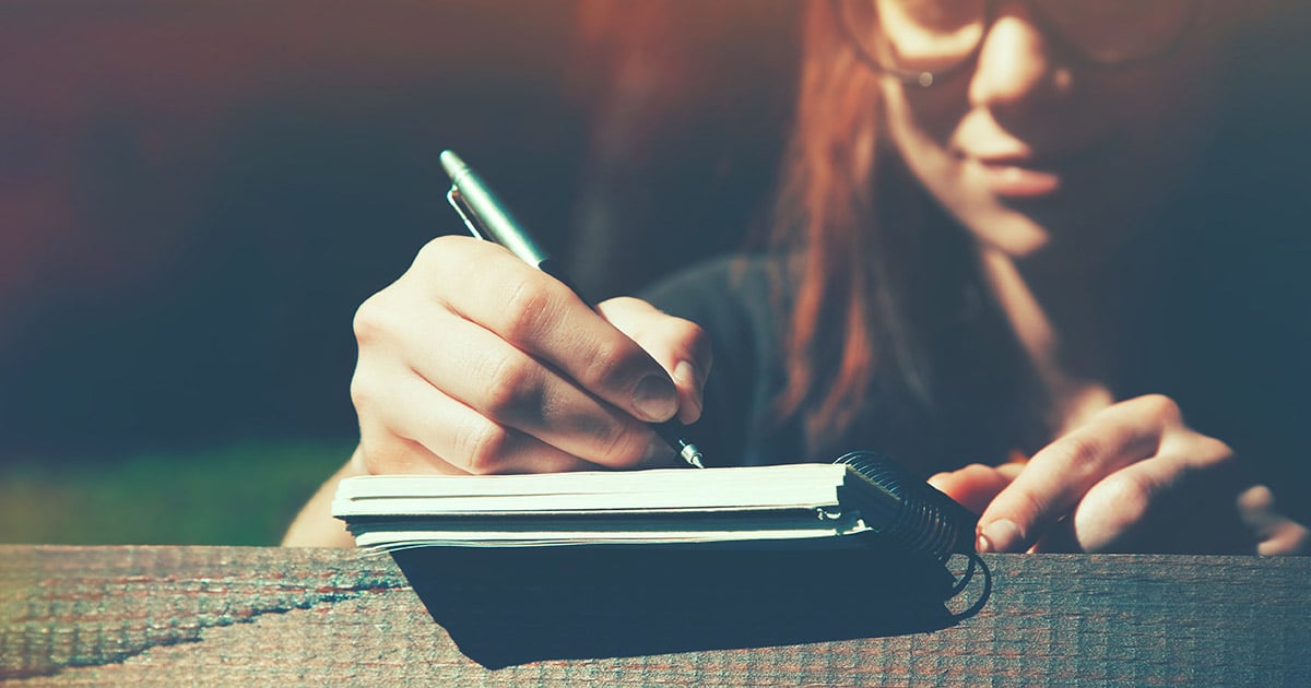 Young woman with glasses writing on a notepad