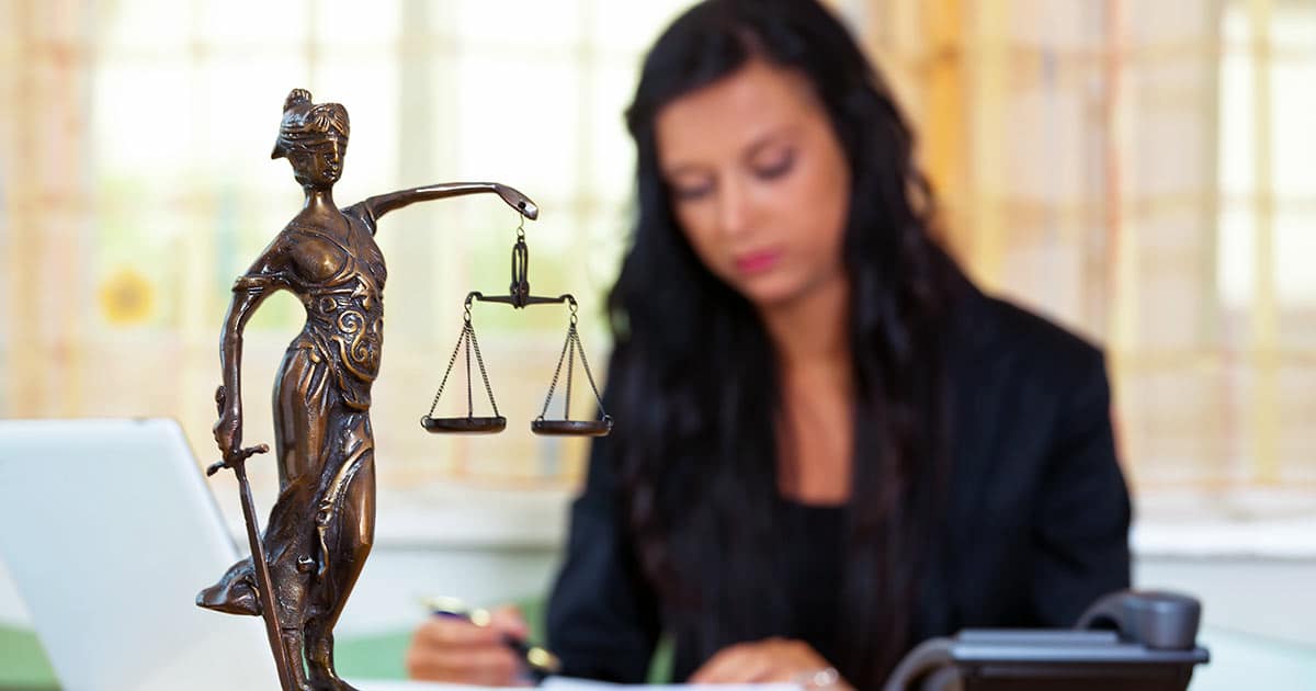 Legal professional sitting behind a blind woman scales of justice statue