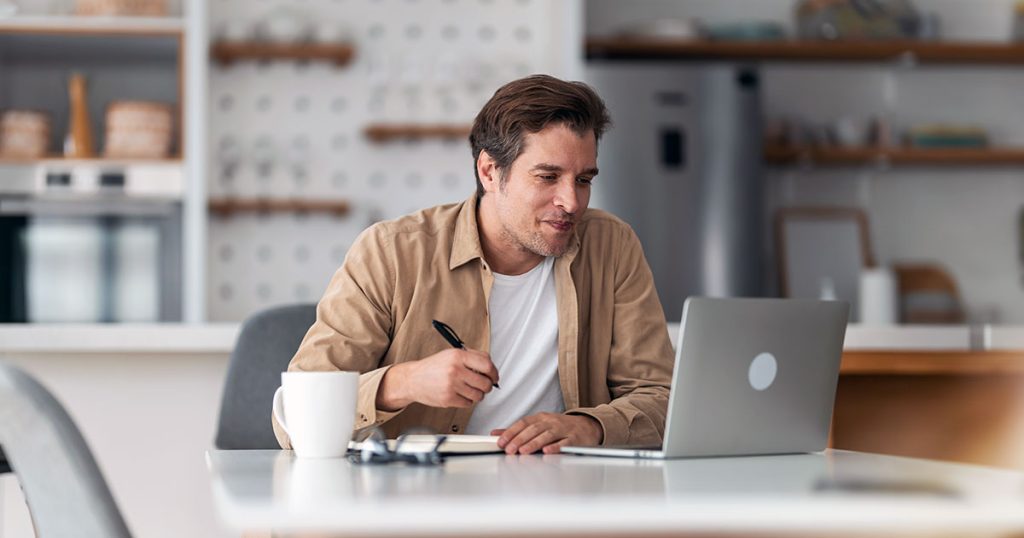 Man taking notes using laptop on kitchen table