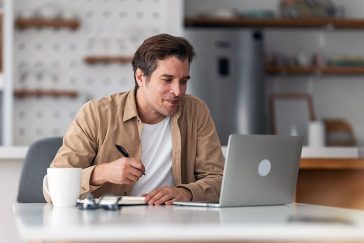 Man taking notes using laptop on kitchen table