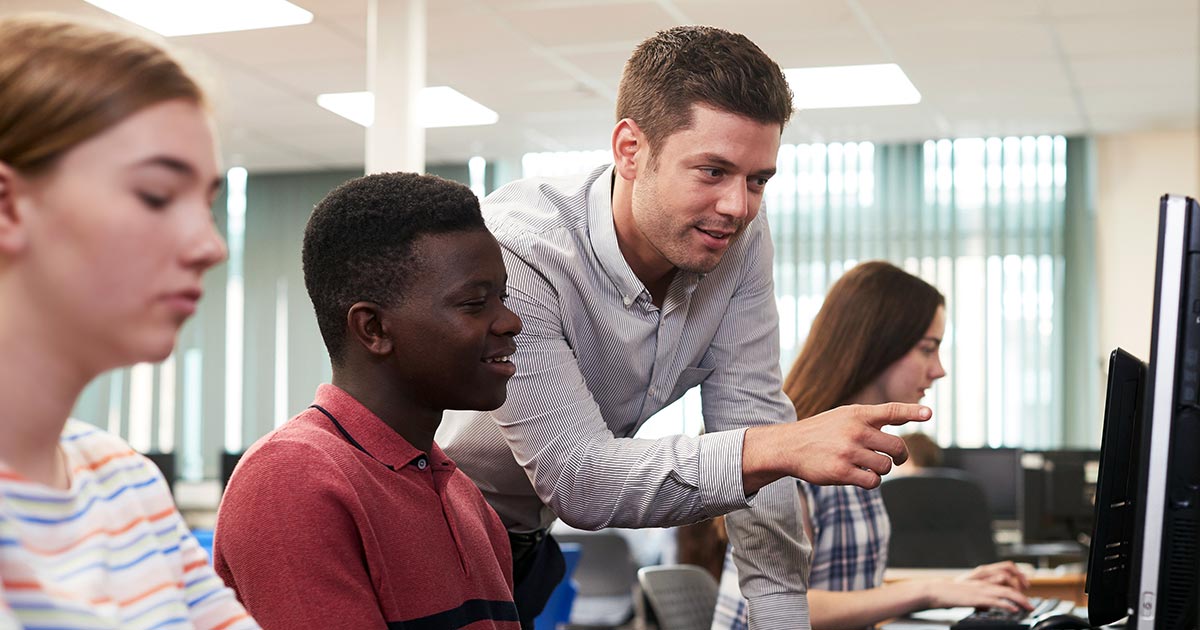 Male educator helping students with computer lab work