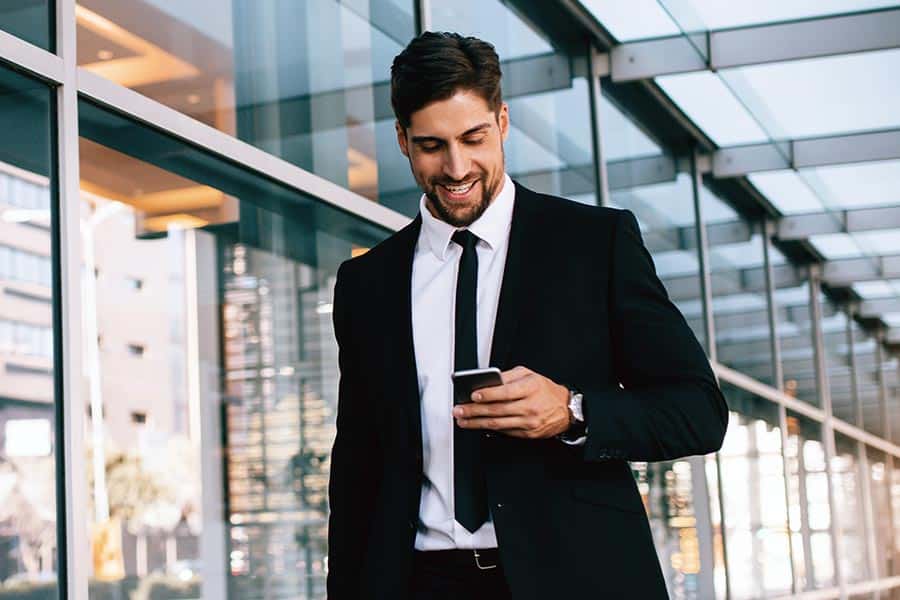 Smiling young businessman walking outside with phone