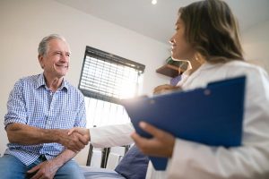 Woman in white with clipboard shaking hand of elderly male patient