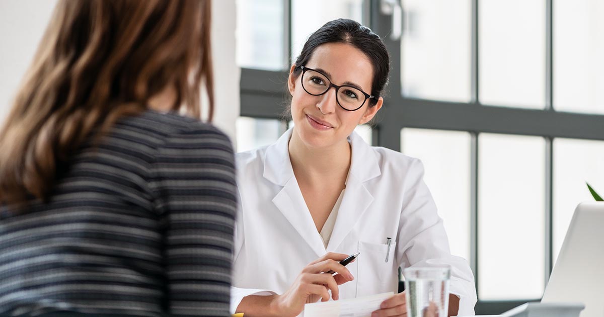 Professional woman in white coat taking notes while talking with another woman