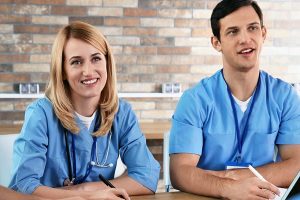 Medical professionals in blue scrubs sitting at table taking notes