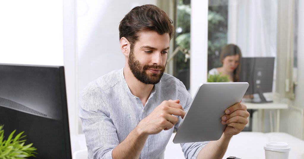 Young man with beard working using multiple devices