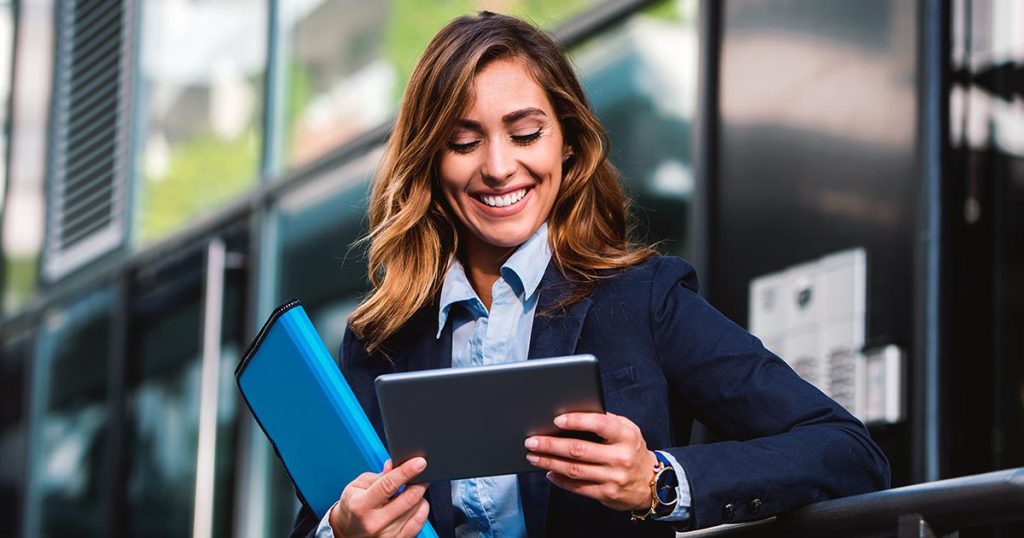 Smiling businesswoman outside building looking at computer tablet
