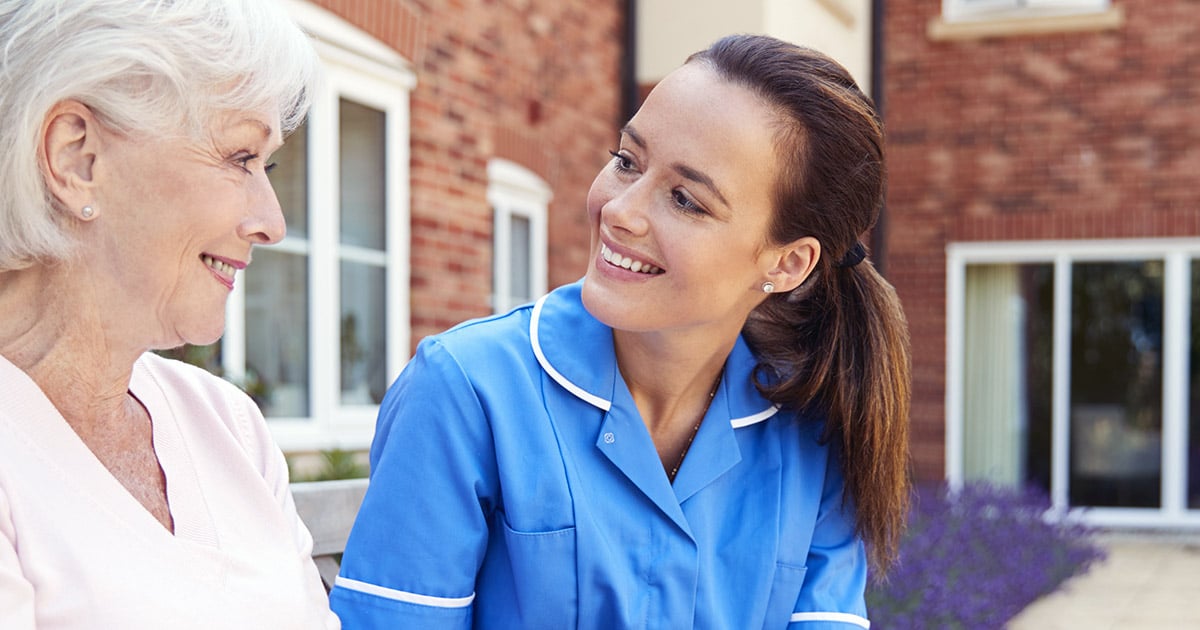 Female nurse wearing blue sitting outside with elderly woman