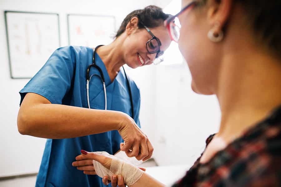 Female nurse applying bandage to wrist of woman patient