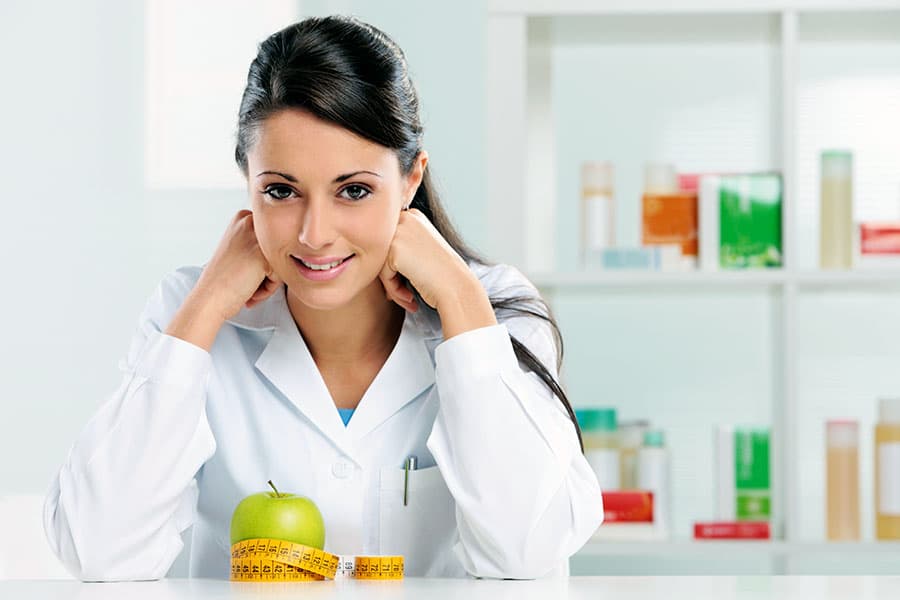 Nutrition expert in white lab-coat in clinical setting with apple and measuring tape