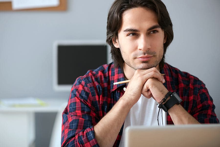 Young man in check shirt contemplating in front of computer