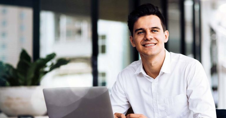 Smiling man in white shirt using laptop