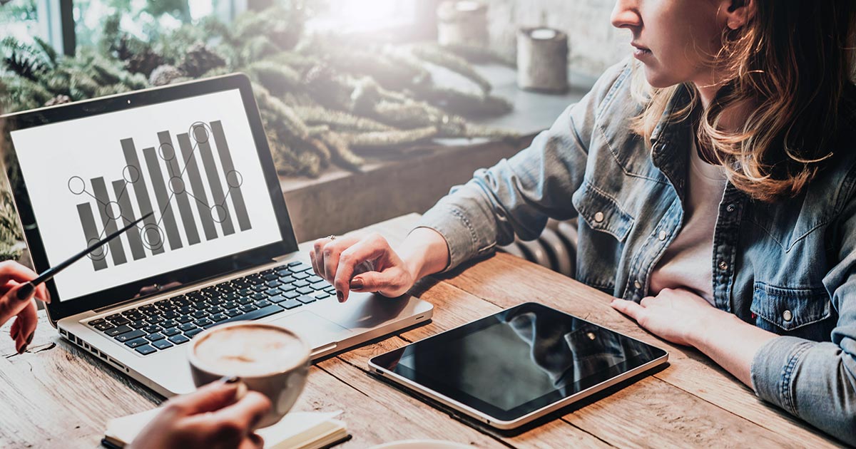 Two people inspecting a chart on a laptop over coffee