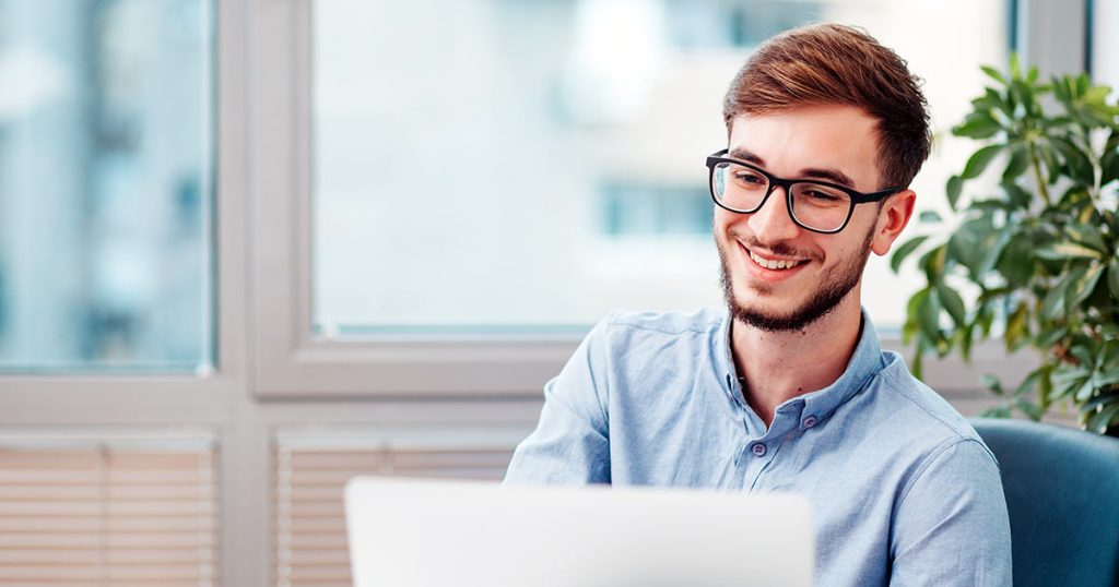 Young man with glasses smiling while using computer