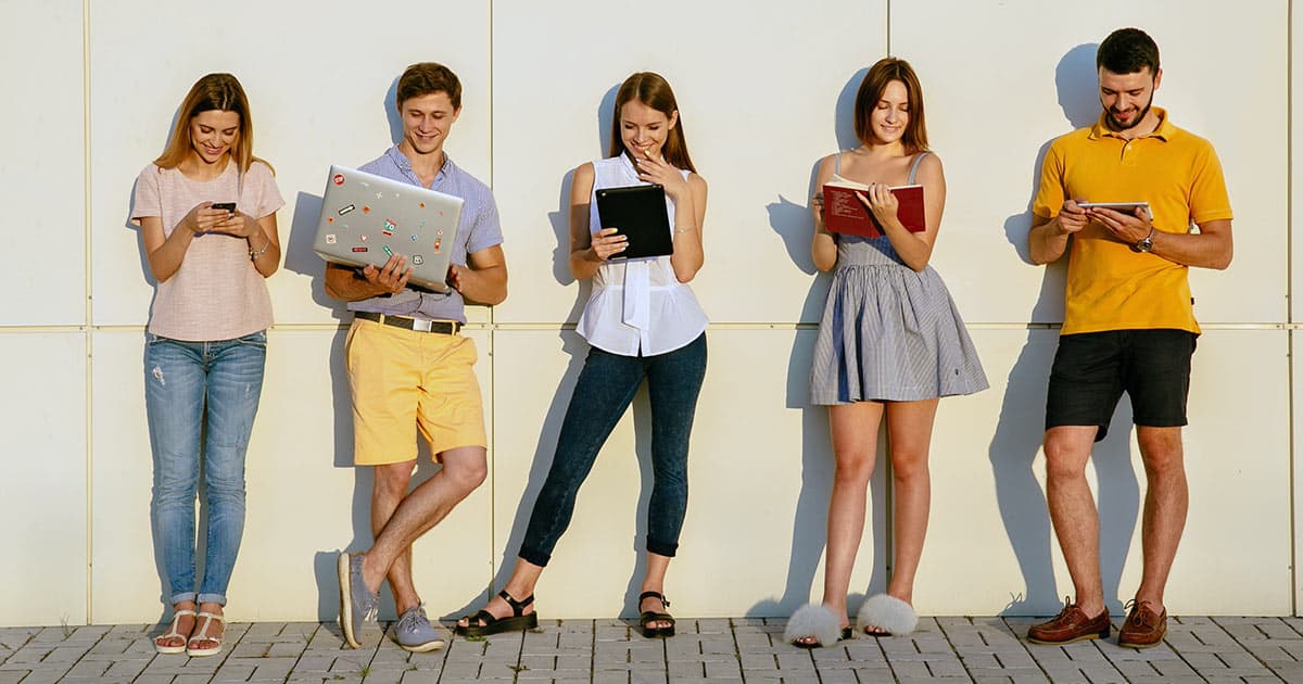 Students standing in a row looking at their devices