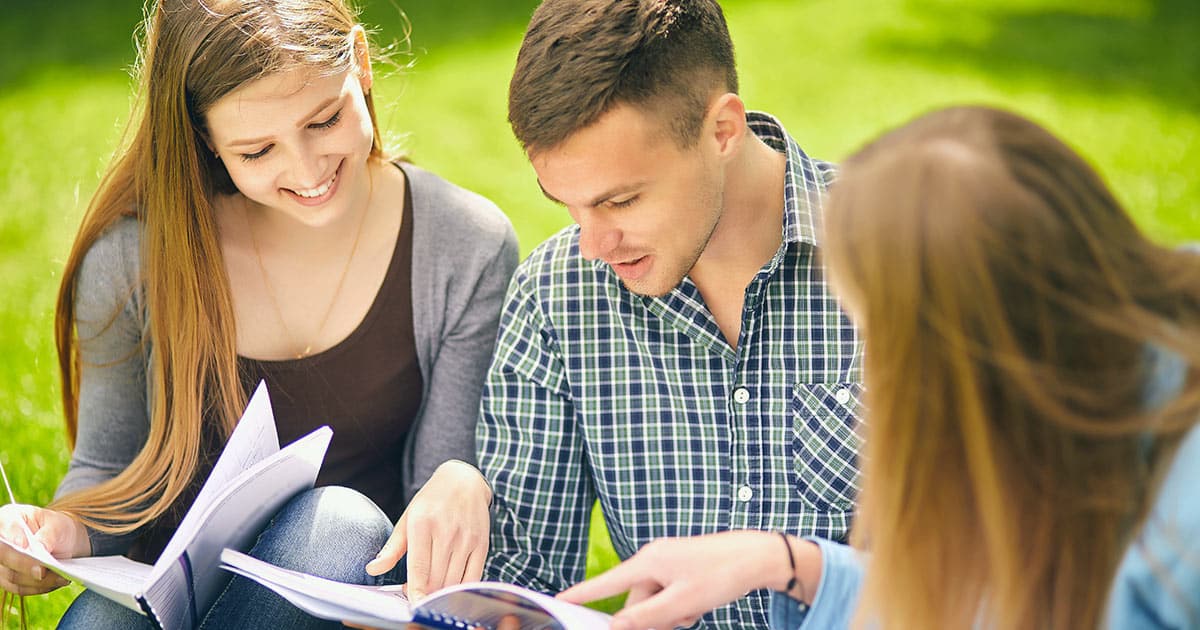 Three young adult students studying on lawn