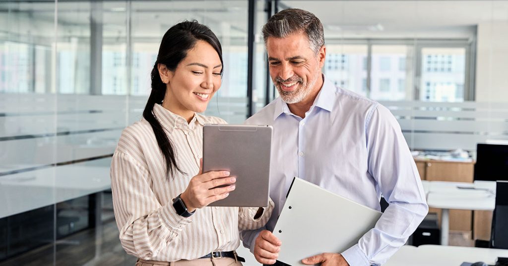 Two business professionals standing to review computer tablet
