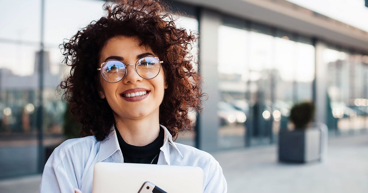 Smiling woman with glasses clutching laptop and tablet